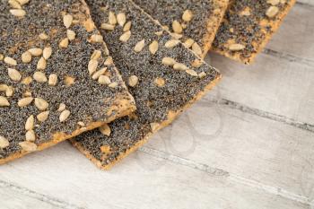 Pile of crackers with poppy and sunflower seeds on gray wooden background.