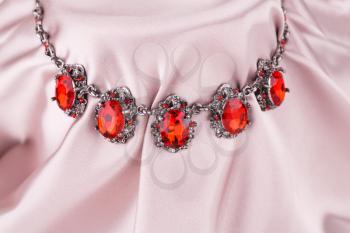 Stylish necklace with red stones on a pink fabric background.