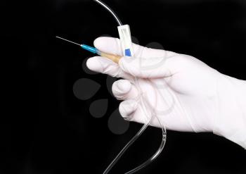 Hand in medical gloves, disposable infusion set. Black background