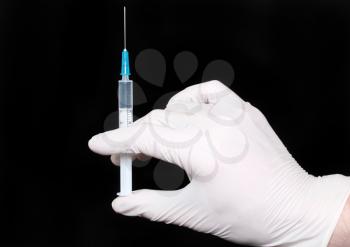 Syringe in a hand in medical gloves, ready for injection with medication. Black background