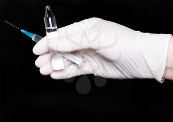 Hands in medical gloves, with ampule and syringe on black background.