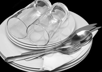 Pile of white plates, glasses with forks and spoons on silk napkin. Black background