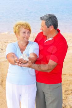 Elderly couple on the coast , holding seashells and corals in his arms.