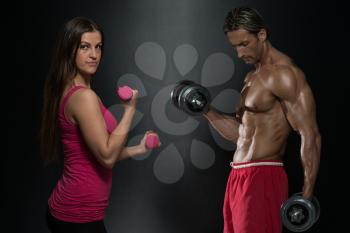Strong Young Couple Working Out With Dumbbells - Shot In Studio On A Black Background