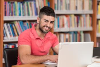 In The Library - Handsome Arabic Male Student With Laptop And Books Working In A High School - University Library - Shallow Depth Of Field