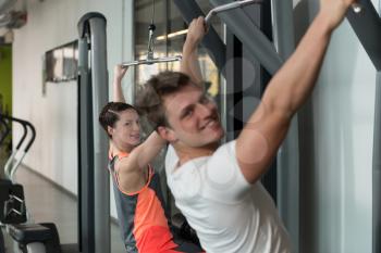 Strong Young Couple Doing Exercise For Back On Machine In The Gym