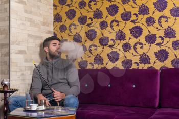 Young Man Smoking Shisha At Arabic Restaurant - Man Exhaling Smoke Inhaling From A Hookah