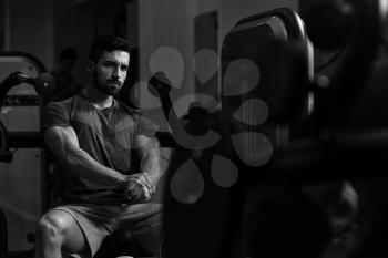 Portrait Of A Young Muscular Athletic Man Posing While Sitting And Showing Bodybuilding Pose In Modern Fitness Center