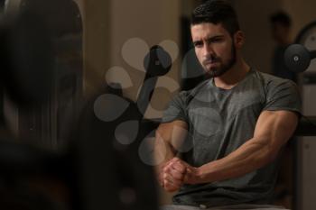Portrait Of A Young Muscular Athletic Man Posing While Sitting And Showing Bodybuilding Pose In Modern Fitness Center