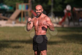 Adult Muscular Sports Guy With A Naked Torso Is Boxing - Doing Street Workout Exercises In Park