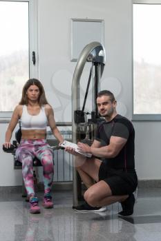 Personal Trainer Showing Young Woman How To Train Triceps On Machine In The Gym
