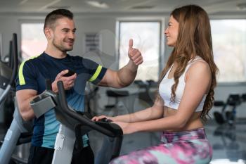 Personal Trainer Showing Ok Sign To Client - Woman Exercising Her Legs Doing Cardio Training On Bicycle