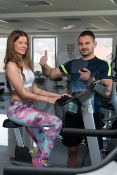 Personal Trainer Showing Ok Sign To Client - Woman Exercising Her Legs Doing Cardio Training On Bicycle