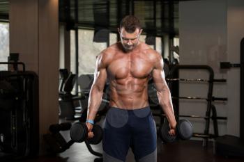 Muscular Man Doing Heavy Weight Exercise For Biceps With Dumbbells In Modern Gym