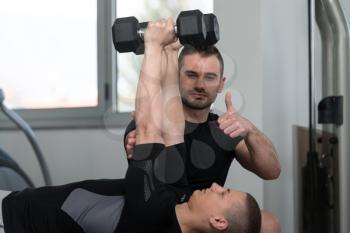 Personal Trainer Showing Ok Sign To Client - Young Man Exercising His Triceps On Machine In The Gym