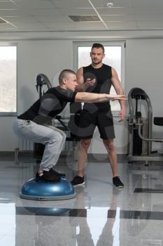 Personal Trainer Showing Young Man How To Train On Bosu Balance Ball In A Gym