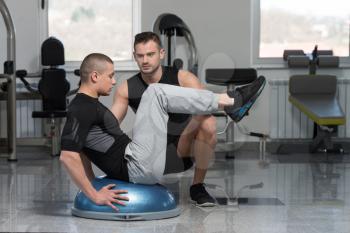 Personal Trainer Showing Young Man How To Train On Bosu Abs Exercise In A Health And Fitness Concept