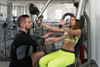 Personal Trainer Showing Young Woman How To Train Chest On Machine In The Gym