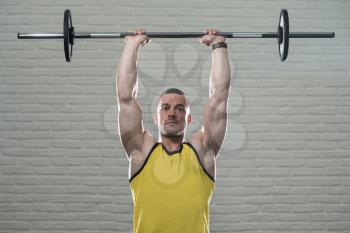 Bodybuilder Working Out Triceps With Barbell On White Bricks Background With Copyspace