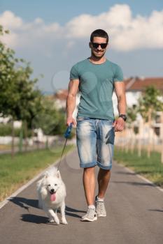 Young Man And German Spitz Walk In The Park - He Keeps The Dog On The Leash