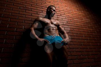 Portrait Of A Young Physically Fit Man Showing His Well Trained Body - Muscular Athletic Bodybuilder Fitness Model Posing After Exercises On Wall of Bricks