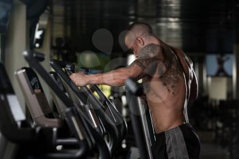 Muscular Young Man Doing Aerobics Elliptical Walker In Modern Fitness Center
