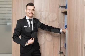 Portrait Of Handsome Confident Young Businessman Standing And Opens Cabinet