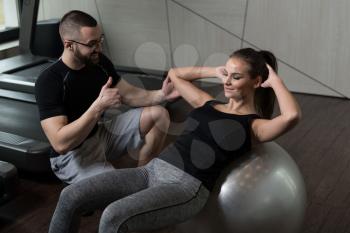 Personal Trainer Showing Young Woman How To Train On Ball Abs Exercise In A Health And Fitness Concept
