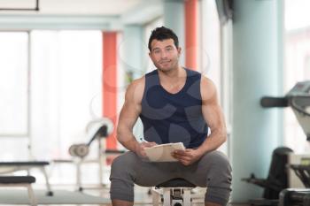 Personal Trainer Takes Notes On Clipboard In a Gym