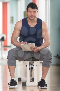 Personal Trainer Takes Notes On Clipboard In a Gym
