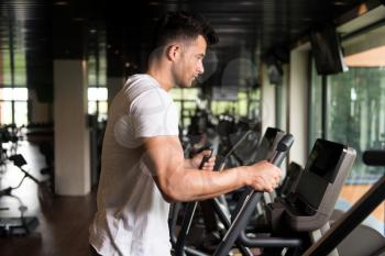 Muscular Man Doing Aerobics Elliptical Walker In Modern Fitness Center