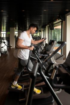 Muscular Man Doing Aerobics Elliptical Walker In Modern Fitness Center