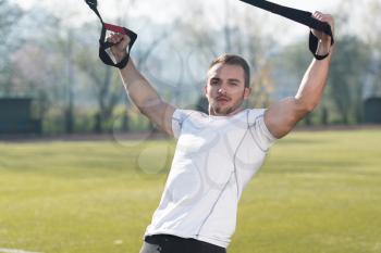Young Man Doing Crossfit With Trx Fitness Straps in City Park Area - Training and Exercising for Endurance - Healthy Lifestyle Concept Outdoor