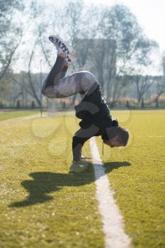 Attractive Man Doing a Hand Stand in City Park Area - Training and Exercising for Endurance - Fitness Healthy Lifestyle Concept Outdoor