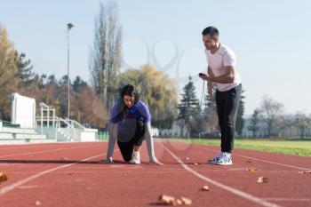 Athletic Personal Trainer Helping Female To Sprint on the Running Track in City Park Area - Training and Exercising for Endurance - Healthy Lifestyle Concept Outdoor