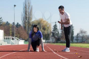 Athletic Personal Trainer Helping Female To Sprint on the Running Track in City Park Area - Training and Exercising for Endurance - Healthy Lifestyle Concept Outdoor