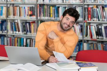 Handsome Male Student With Laptop and Books Working in a High School Library