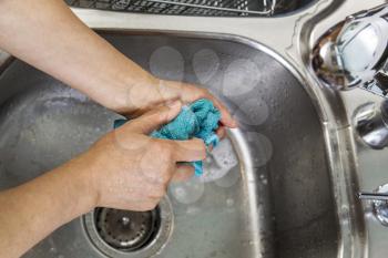 Hands cleaning dish rag with soapy suds in kitchen sink