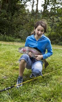 Preteen girl expressing happiness after catching trophy trout with trees and sky in background