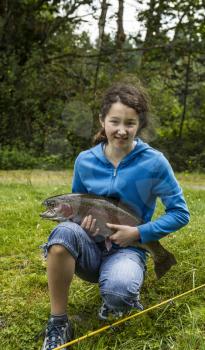 Young girl holding trophy rainbow trout with trees and sky in background