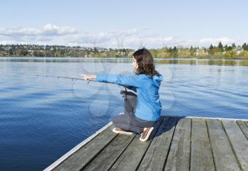Girl pointing at feeding fish on lake while fishing from wooden dock
