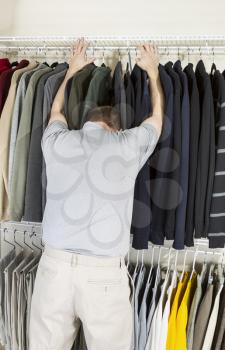 Vertical portrait of mature man in walk-in closet sticking his head in sweaters due to being tired