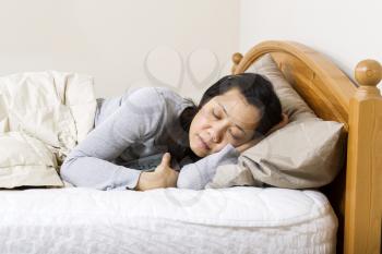 Horizontal photo of mature woman, lying head down in pillow, while holding alarm clock next to her