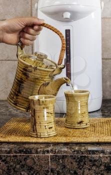 Hand pouring tea into cup on kitchen counter top with hot water dispenser in background