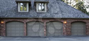 Four car garage doors made of wood and brick with trees and sky in background
