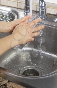 Vertical photo of female hands rinsing a drinking glass with water running from kitchen faucet sink