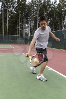 Young Asian Man using single handed backhand on outdoor tennis court