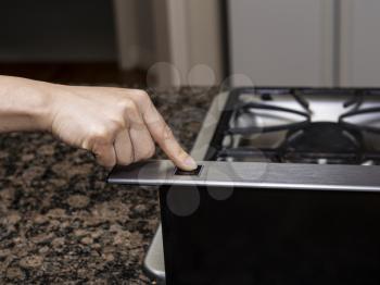 Index finger pushing fan button on top of gas stove range
