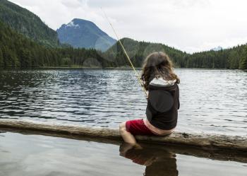 Young girl fishing off log into mountain lake in Washington State