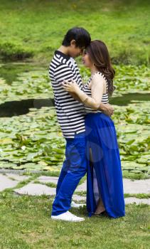 Vertical photo of young adult couple holding each other very closely with the lily pond in background  